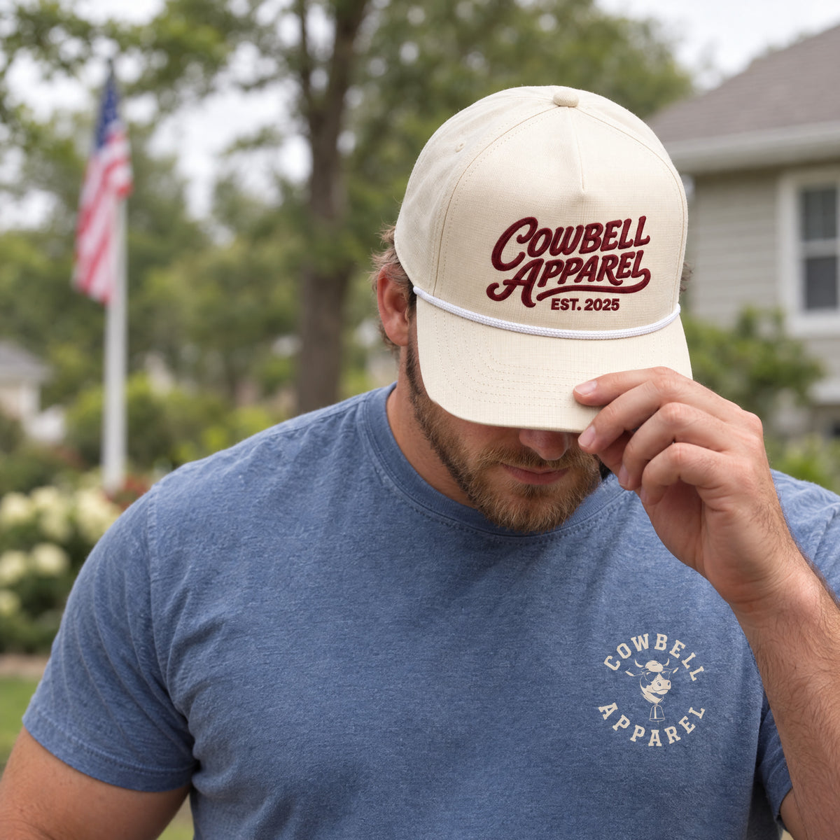 A man in a Cowbell Apparel rope hat and Cowbell tee in his backyard with an American flag behind him